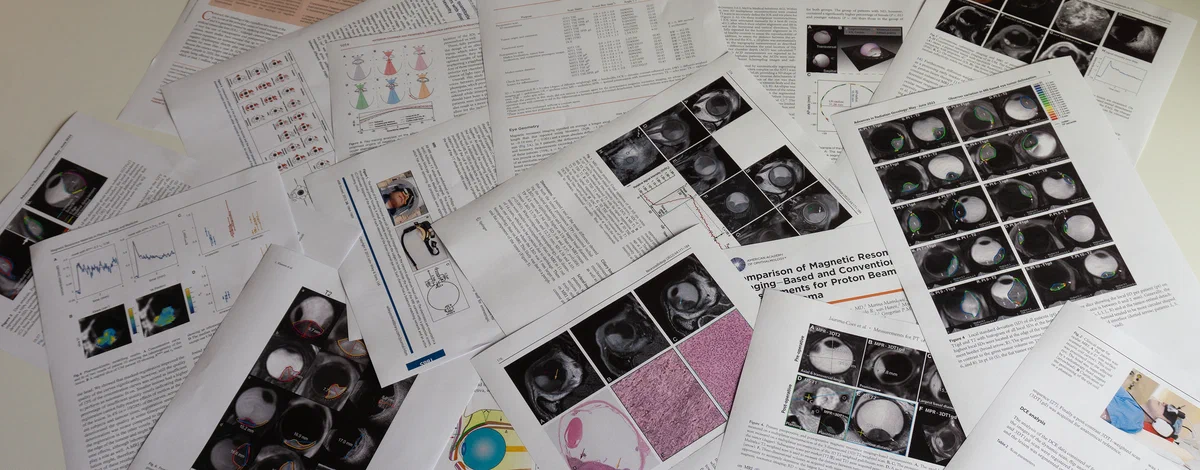 Stack of scientific journals and papers from the MReye research group